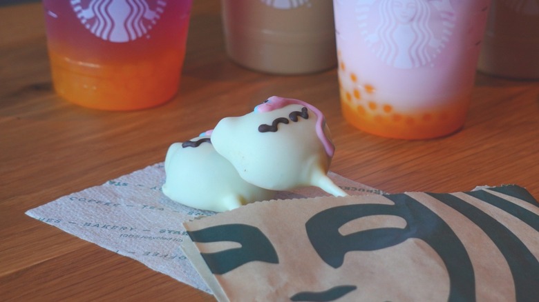 Two of Starbucks' Unicorn Cake Pops placed on top of one another in a bakery item bag in front of Starbucks beverages.