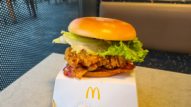 A McDonald's Spicy Deluxe McCrispy sits on top of a takeaway box