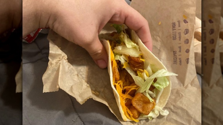 A person holds a Taco Bell Spicy Potato Soft Taco