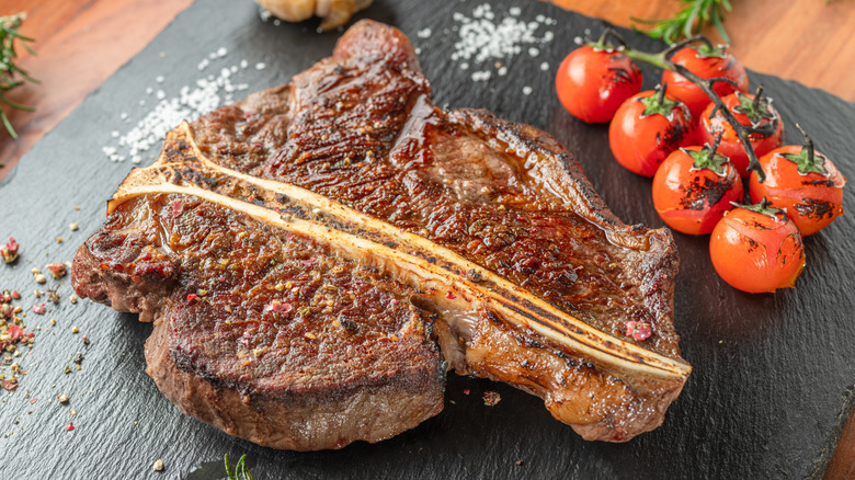 A seared T-bone steak on a black plate.