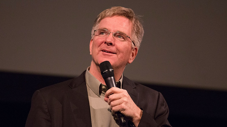 Rick Steves holds a mic up and gazes upward and outward