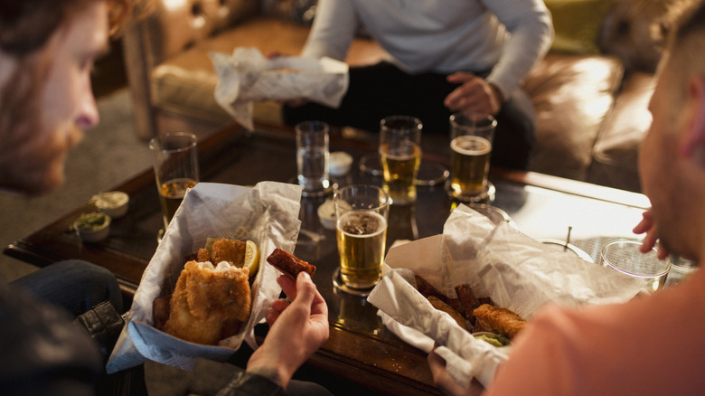 Group of men eating fish and chips and drinking beer at a table.