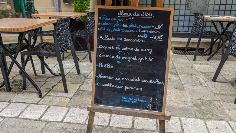 Chalkboard menu outside a European restaurant with tables in the background