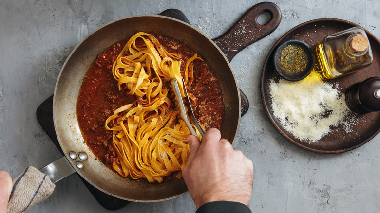 Person tossing pasta with sauce