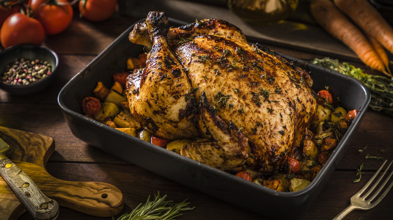 Roast chicken on a bed of vegetables in a baking dish