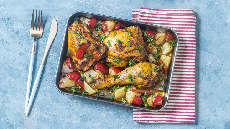 Tray of roast chicken on a bed of root veggies next to a napkin and silverware