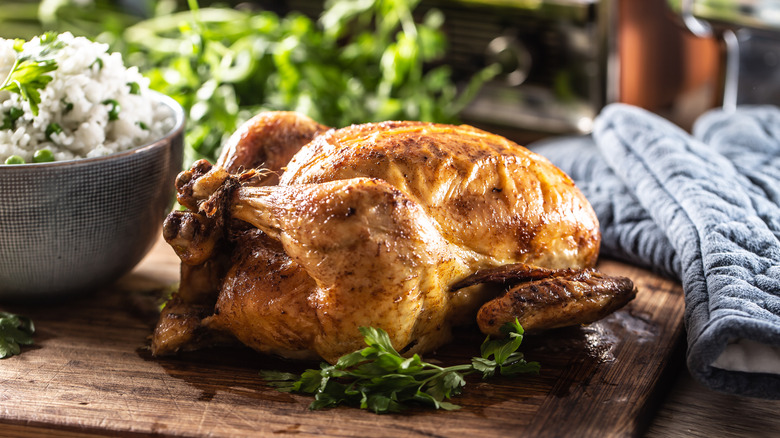 A whole roast chicken with a big bowl of rice and peas