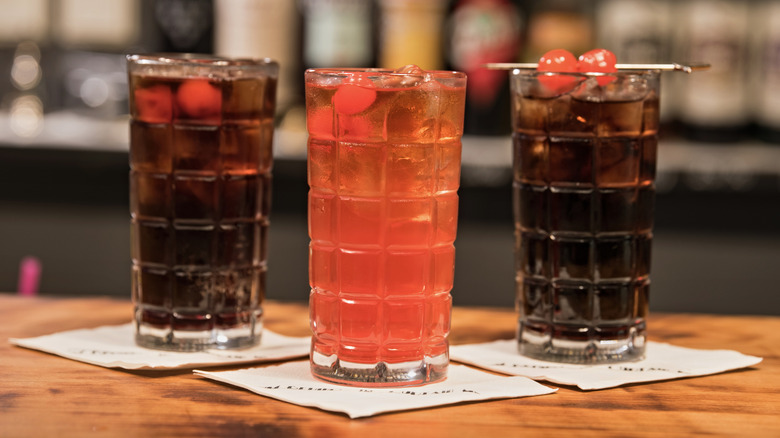 Soda cocktails in tall glasses with maraschino cherries on napkins in a bar
