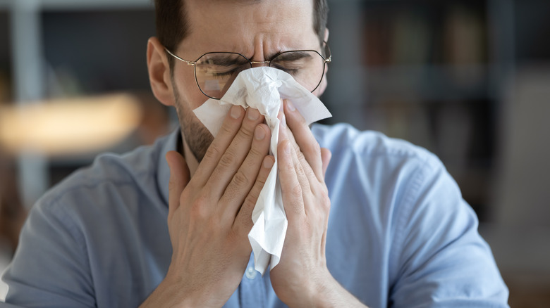 Man with a tissue held up to face who is likely sick