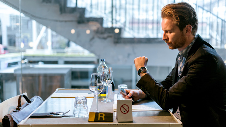 Man sitting at restaurant table looking at watch