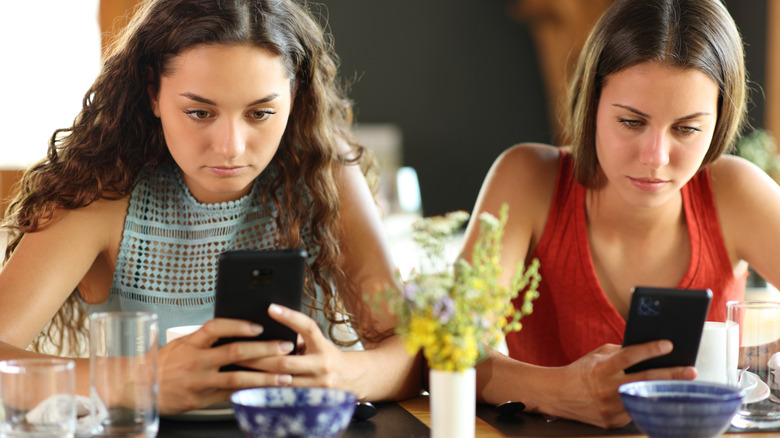 Two girls on their phones not talking to one another while dining out