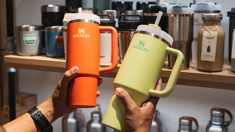 Orange and yellow Stanley Cups held in person's hands.