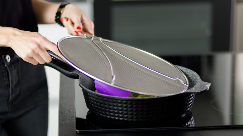Person placing splatter guard over skillet