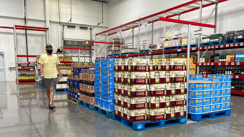 A man wearing a mask walks among the cases of beer in a Sam's Club
