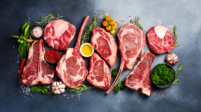 A variety of raw beef cuts surrounded by aromatics