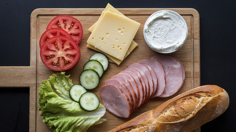 A variety of sandwich ingredients sit on a wooden cutting board