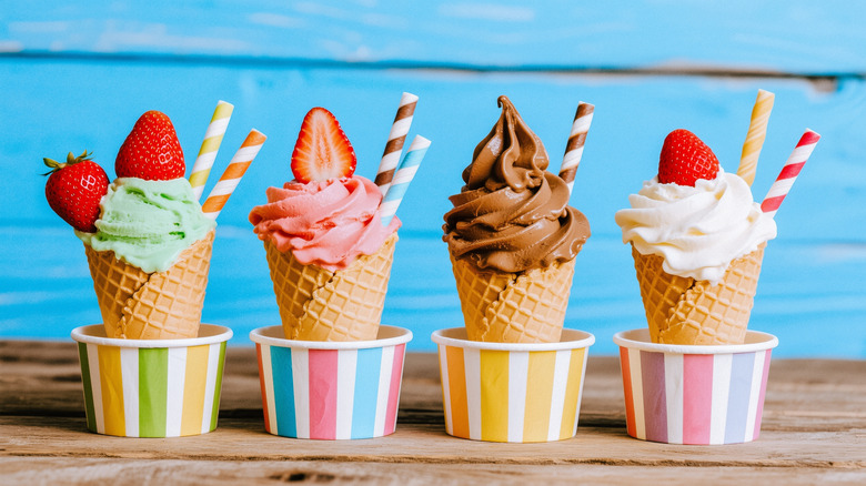 Four ice cream cones (mint, strawberry, chocolate, and vanilla) topped with strawberry and inside of cones in front of a blue background and placed on a wooden table