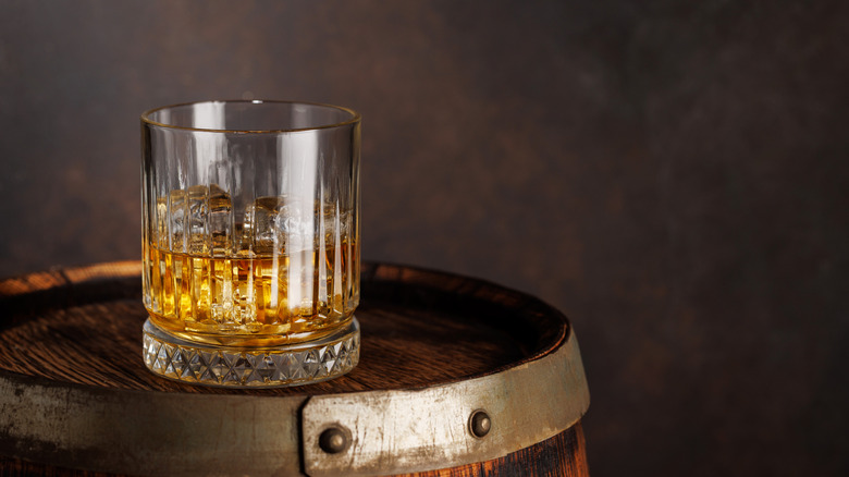 A glass of Scotch on an oak barrel.