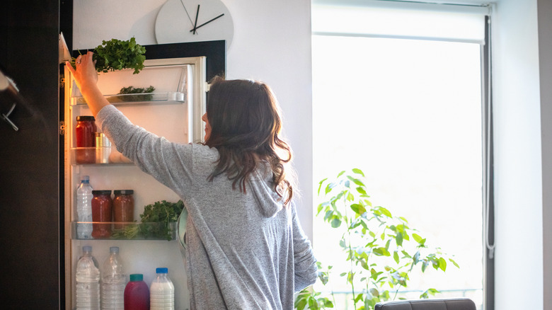 woman pulling greens from refrigerator