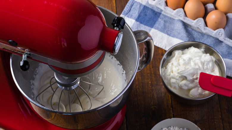 red mixer on wooden table with cream and eggs