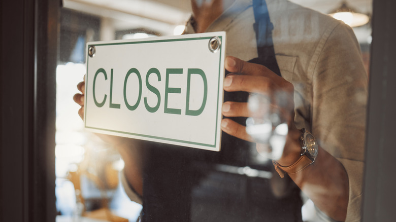 A person hangs a closed sign in the window of a restaurant