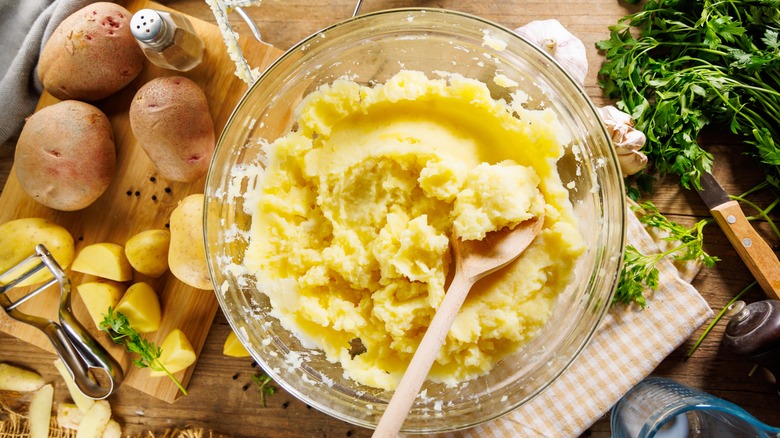 A bowl of homemade mashed potatoes, surrounded by extra ingredients and kitchen tools