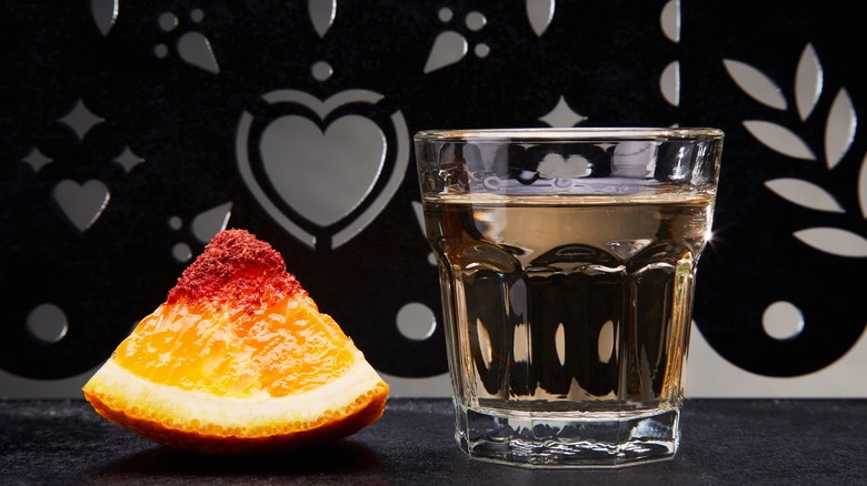 A glass of mezcal with a chili salt rimmed chunk of orange