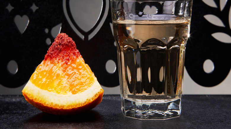 A glass of mezcal with a chili salt rimmed chunk of orange