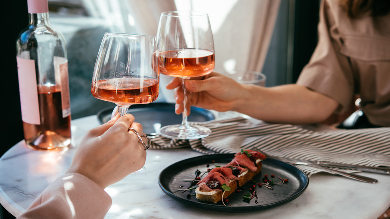 Hands clinking glasses of rosé in a restaurant