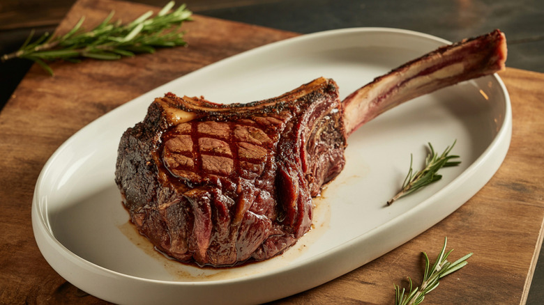 A tomahawk steak sits on a plate, ready to eat.