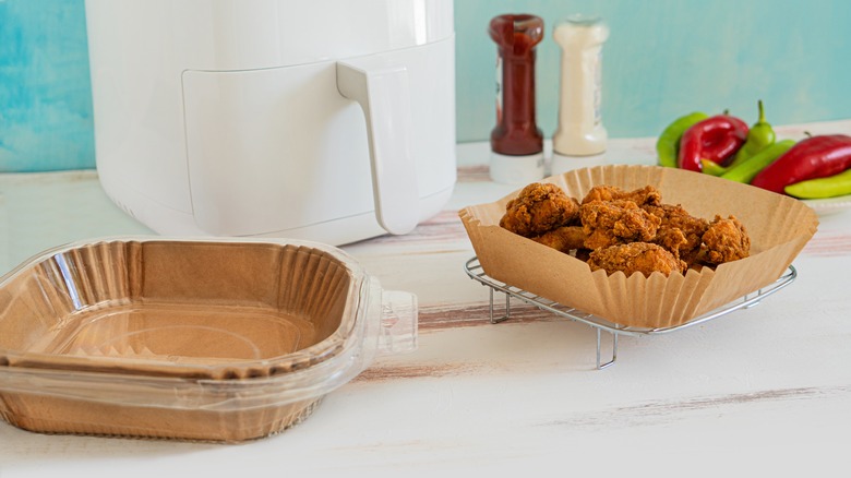 Fried chicken cools in a air fryer liner outside of a white air fryer