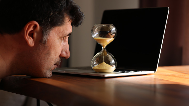 Man staring at an hourglass and waiting for time to pass