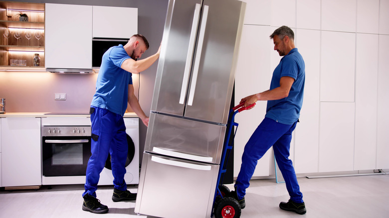 Two men in blue uniforms delivering a new fridge