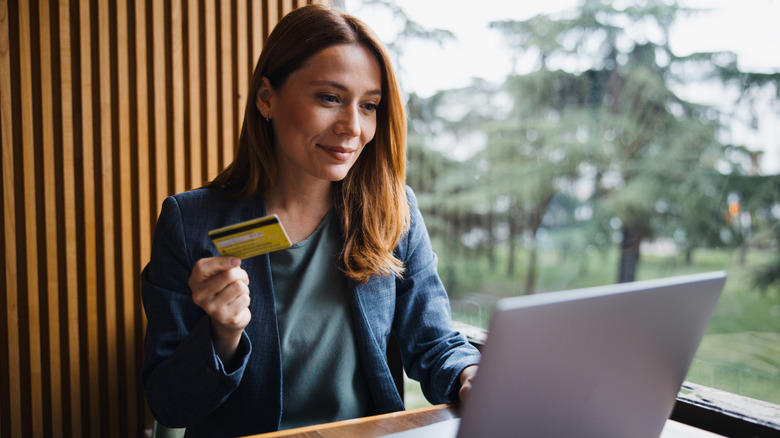 Woman holding credit card while sitting n front of an open laptop