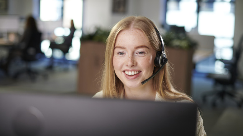 Smiling woman wearing a headset and taking calls in front of a computer