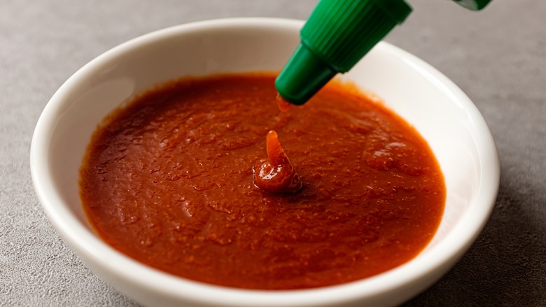 sriracha sauce being poured from a bottle into a small white ceramic bowl