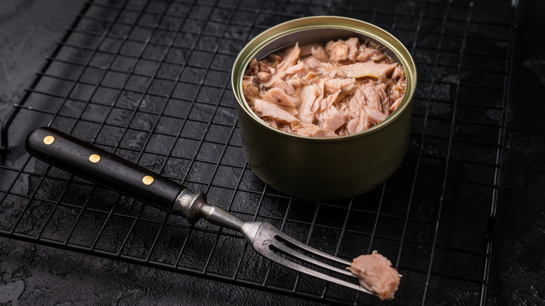 Open can of tuna on black table with fork