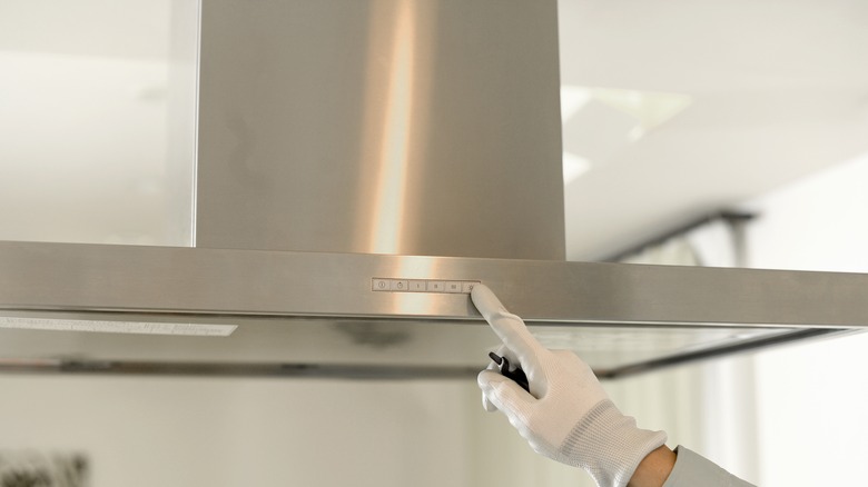 An inspector's gloved hand touches a stove's range hood