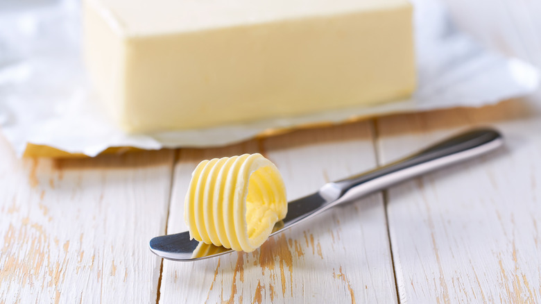 Butter on knife in front of butter block on wrapper