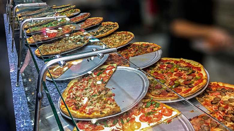 Large selection of pizza slices with various toppings at a pizzeria