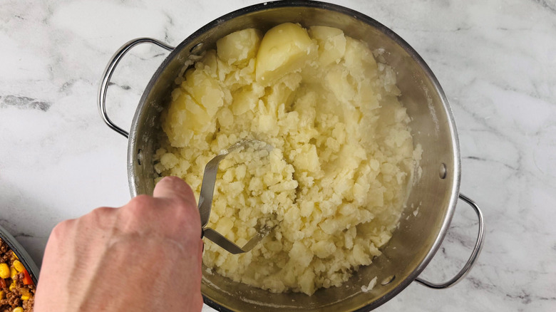 Hand using potato masher to mash potatoes in large pot