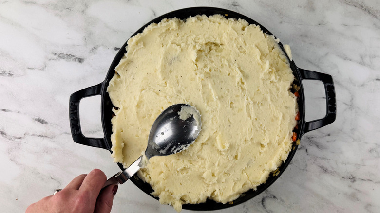 Spoon smoothing mashed potatoes over pan