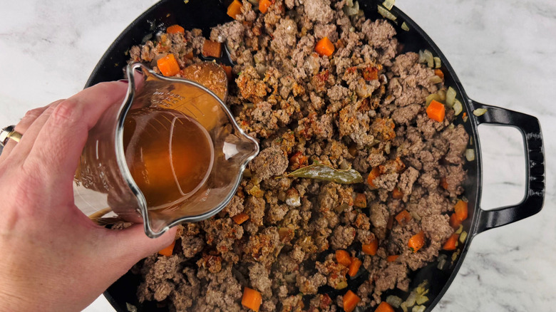 Hand pouring liquid into shepherd's pie filling mixture