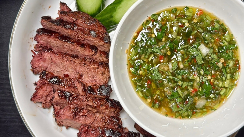 Jeow som sauce being in a small glass bowl next to sliced vegan steak.