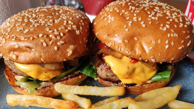 Lamb-based cheeseburgers sit next to each other with some fries.