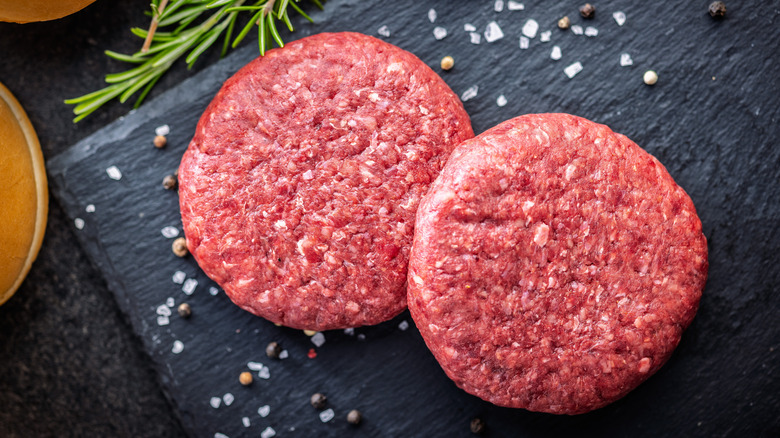 Burger patties resting on a cutting board.