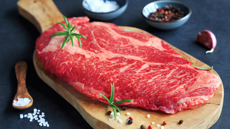 A raw chuck steak on a wooden board.