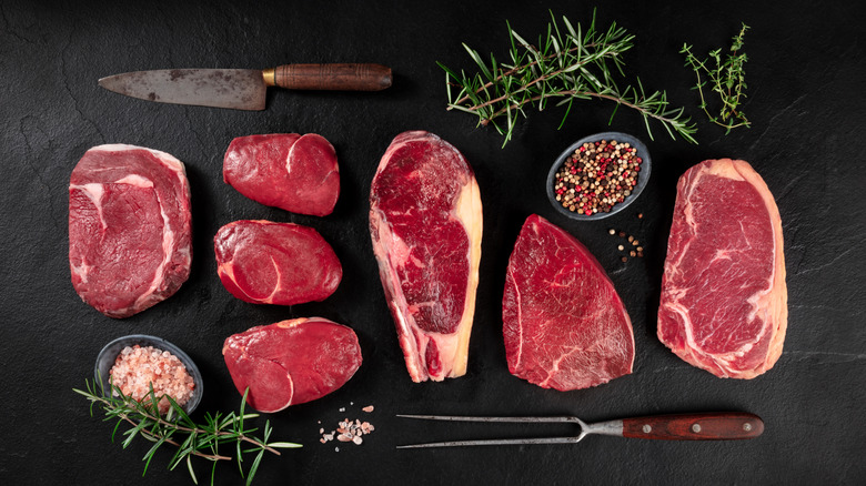 A variety of steak cuts sit on a black surface.