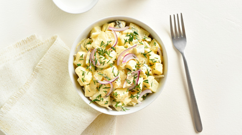 A bowl of potato salad with onion and herbs.
