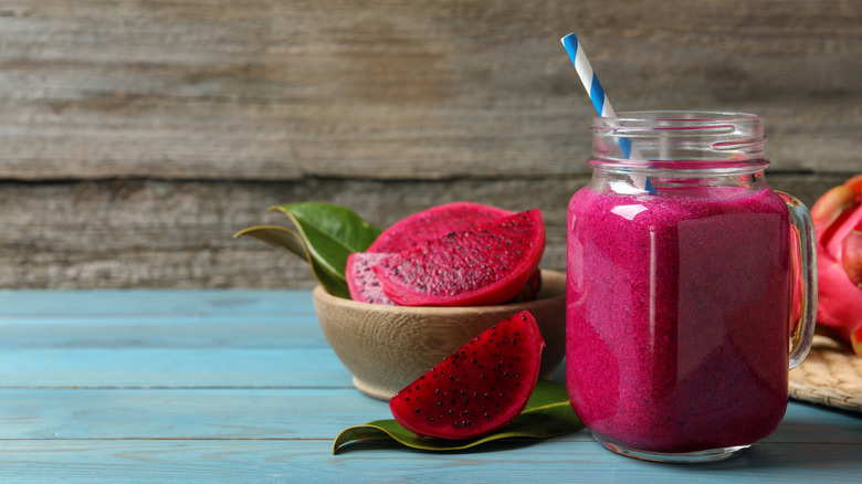 Pink dragonfruit smoothie in a mason jar glass with a straw and fresh dragonfruit on the side